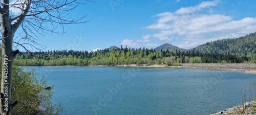 Obraz na płótnie A wide shot captures the serene Lake Lepenica in Gorski Kotar, surrounded by lush green forests and distant mountains under a bright blue sky with scattered clouds w salonie