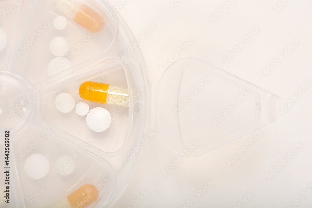 A close-up shows a section of a clear plastic pill organizer containing various white round pills and yellow and white capsules