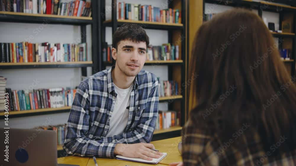 Young man engaged in a thoughtful conversation with a woman in a cozy library setting during the day, surrounded by books and a friendly atmosphere Young man engaged in a thoughtful conversation with a woman in a cozy library setting during the day, surrounded by books and a friendly atmosphere