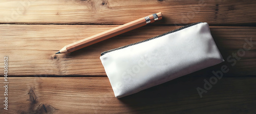 A blank pencil case lying on a wooden table. The side is empty for branding. Sleek design, stylish, well-lit setting. 