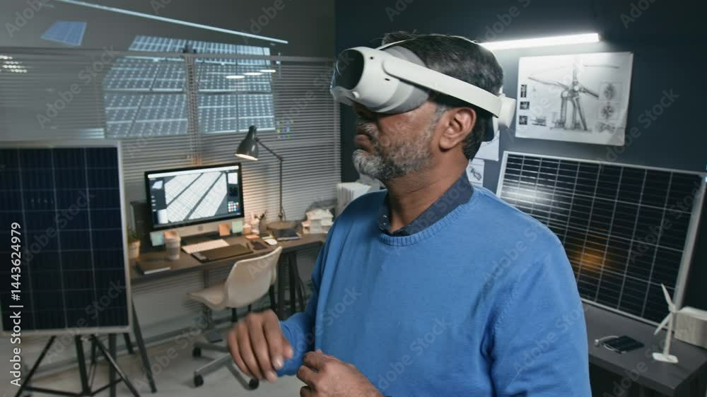 Chest up shot of senior male engineer wearing augmented reality headset and enhancing solar power system at site at renewable energy office with technical drawing, solar panels and computer in back
