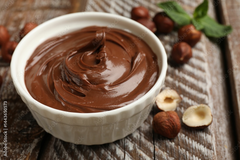 Chocolate hazelnut spread in bowl, nuts and mint on wooden table, closeup Chocolate hazelnut spread in bowl, nuts and mint on wooden table, closeup