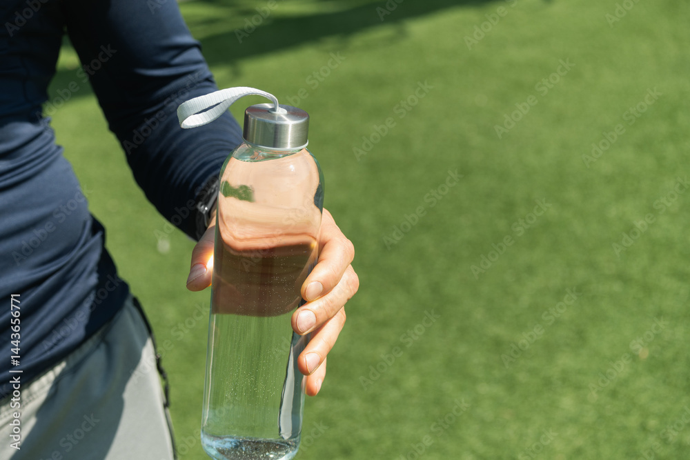 Water bottle in man hand on outdoor sports ground. Concept water balance for heat season for workout. Close up.