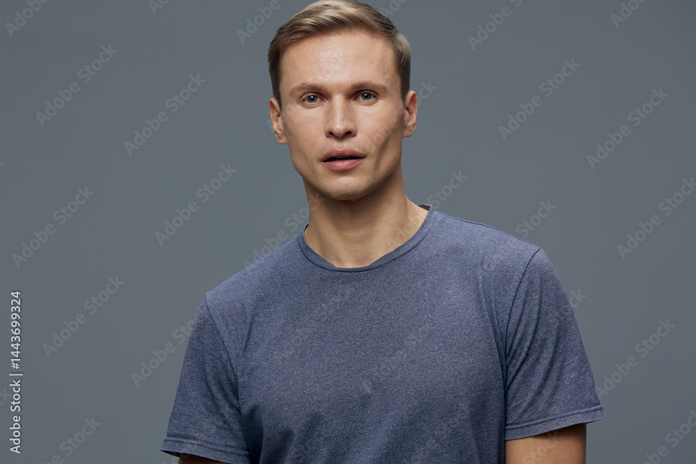 Close-up of a young man with short hair and light skin wearing a blue t-shirt against a plain gray background. Studio portrait, human face, casual clothing, natural expression, simple background, male Close-up of a young man with short hair and light skin wearing a blue t-shirt against a plain gray background. Studio portrait, human face, casual clothing, natural expression, simple background, male
