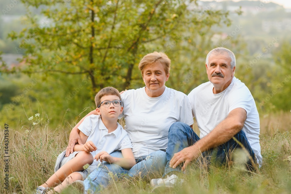 Grandson, grandfather and grandmother sitting on grass having fun outdoors in park at sunset Grandson, grandfather and grandmother sitting on grass having fun outdoors in park at sunset
