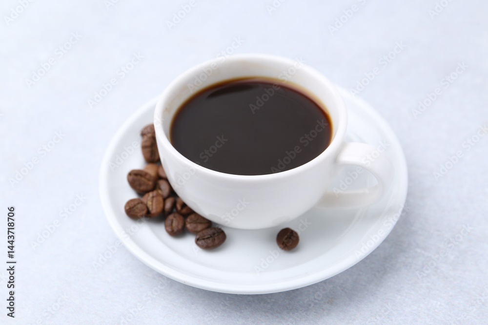 Aromatic coffee in cup, beans and saucer on light table, closeup