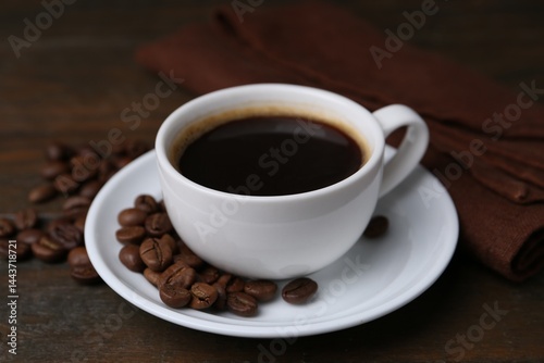 Aromatic coffee in cup, beans and saucer on wooden table, closeup