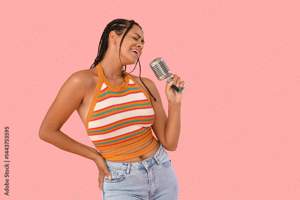 Beautiful African-American woman with microphone singing on pink background
