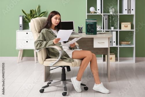 Beautiful young woman working and using portable table fan with humidifier in office
