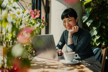 Businesswoman working on laptop in a sunny cafe, enjoying coffee and plants