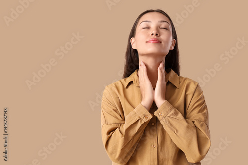 Young Asian woman self-examining thyroid gland on beige background photo
