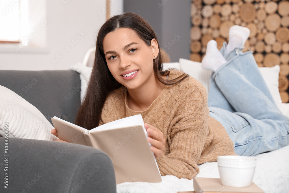 Beautiful young happy woman reading book on sofa at home