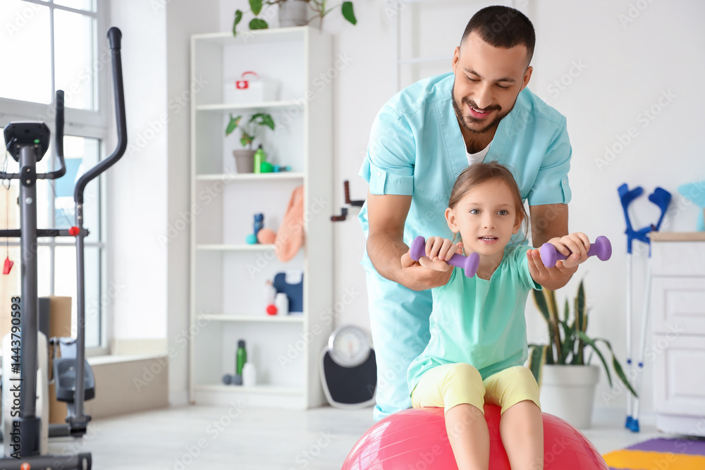 Male physiotherapist and little girl with dumbbells training on fitball in rehabilitation center