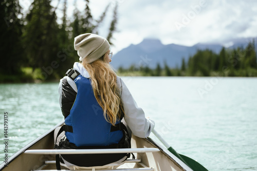 Backview of adventurous young woman canoeing in Banff with mountains and copy space