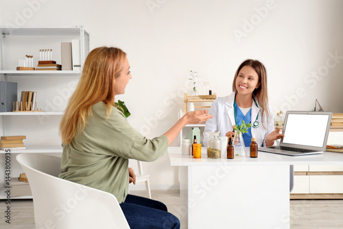 Female homeopathic doctor with laptop and patient at table in office