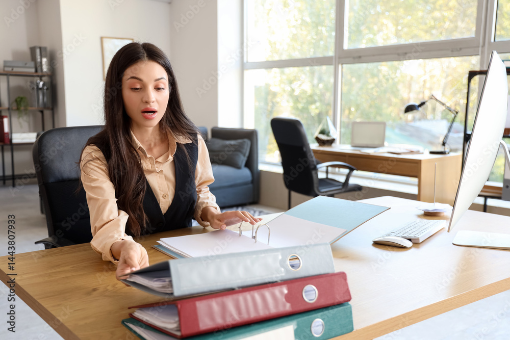 Shocked businesswoman with folders at desk in office