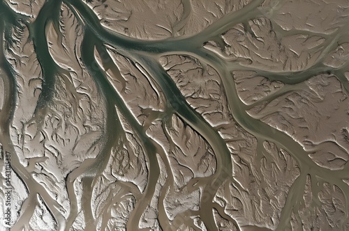 Abstract aerial top-down view of intricate tidal estuary patterns, showing the contrast between water channels and textured mudflats or marshes, natur