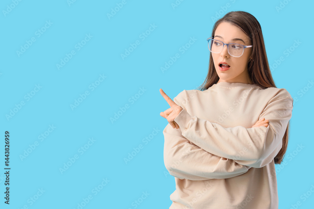 Wondering young woman pointing at something on blue background Wondering young woman pointing at something on blue background