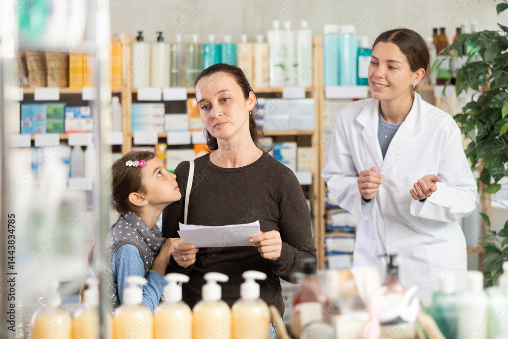 Obraz premium Mother and girl with prescription looks at assortment, bored child pull mother by hand. Client has poor understanding of range and looks for familiar package of medicine. Pharmacist offer consultation
