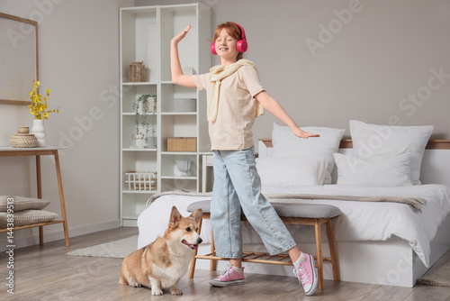 Teenage redhead girl with headphones and cute Corgi dog dancing in bedroom