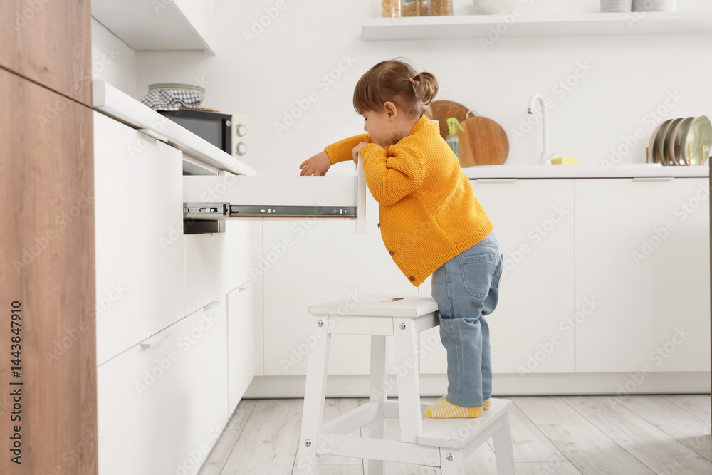 Cute little girl with open drawer in kitchen. Child at risk