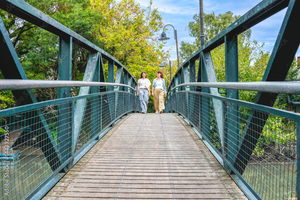 Obraz premium Women sharing laughter as they stroll over a beautiful bridge