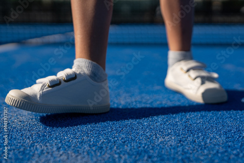 Bild auf Leinwand Close-up of white velcro sneakers on blue padel court surface with soft sunlight