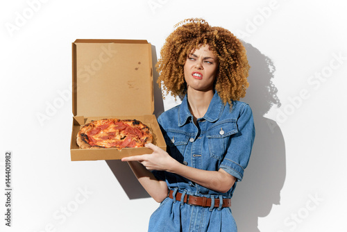 Young woman with curly hair showing distaste holding a pizza box against a white background The emotional expression reflects disappointment