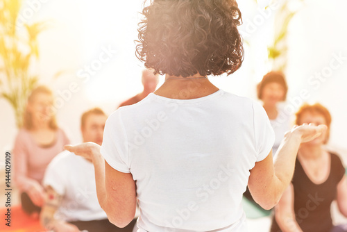 Rear view of a yoga instructor giving a lesson to a class in a health and wellness center. Female teacher giving an instructional lesson on meditation techniques to her students in a meditating class