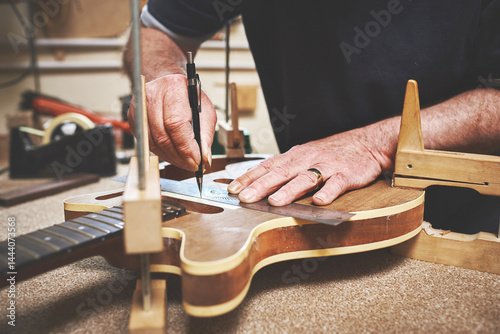 Closeup of man hands repairing, fixing and building a guitar in luthiers service workshop. Professional male standing, measuring and servicing music instrument on workbench in his garage.