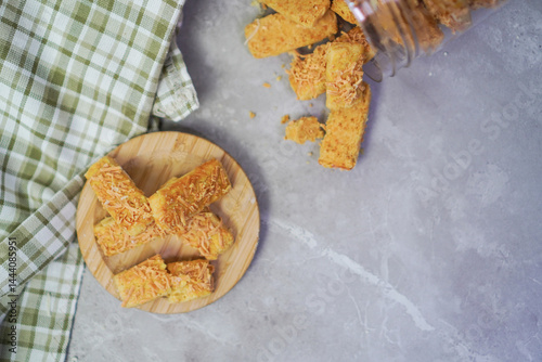 top view of cheese cookies on a wooden coaster, with gingham fabric and cookie jar open and lying nearby