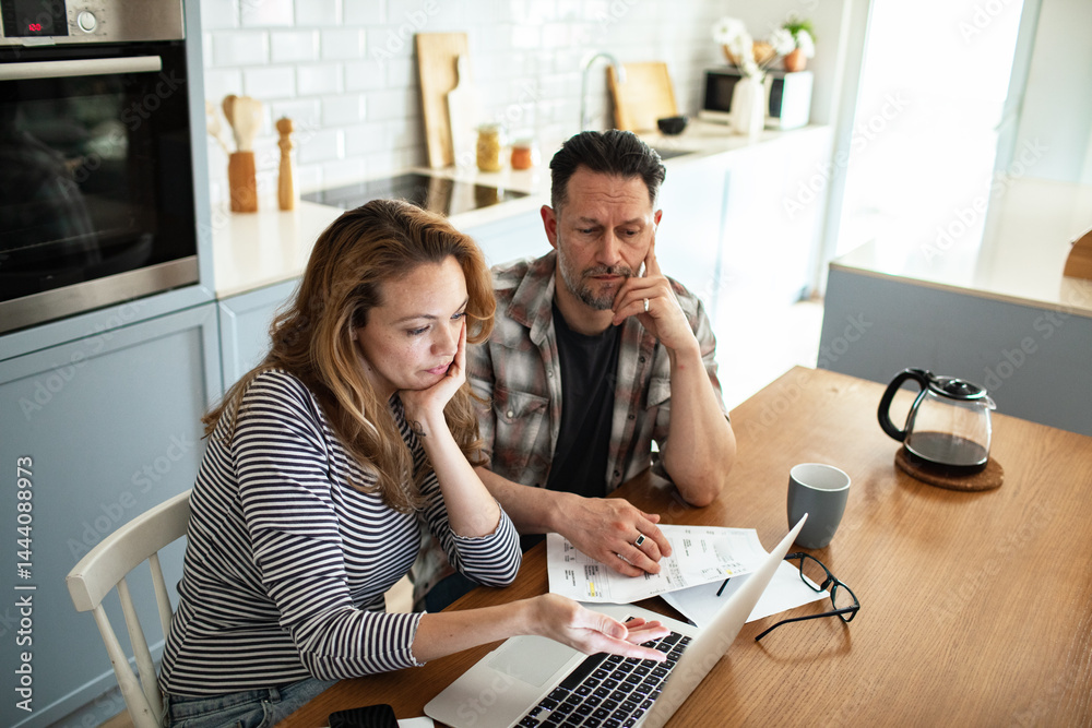 Couple reviewing household finances and bills on laptop in kitchen