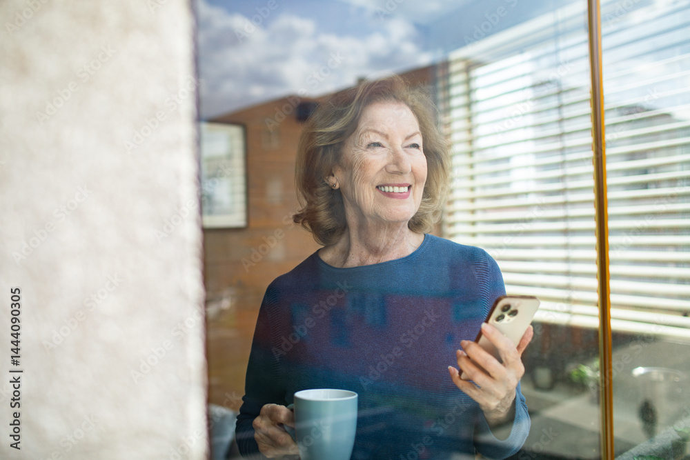 Senior woman smiling while using smartphone at home in bright living room