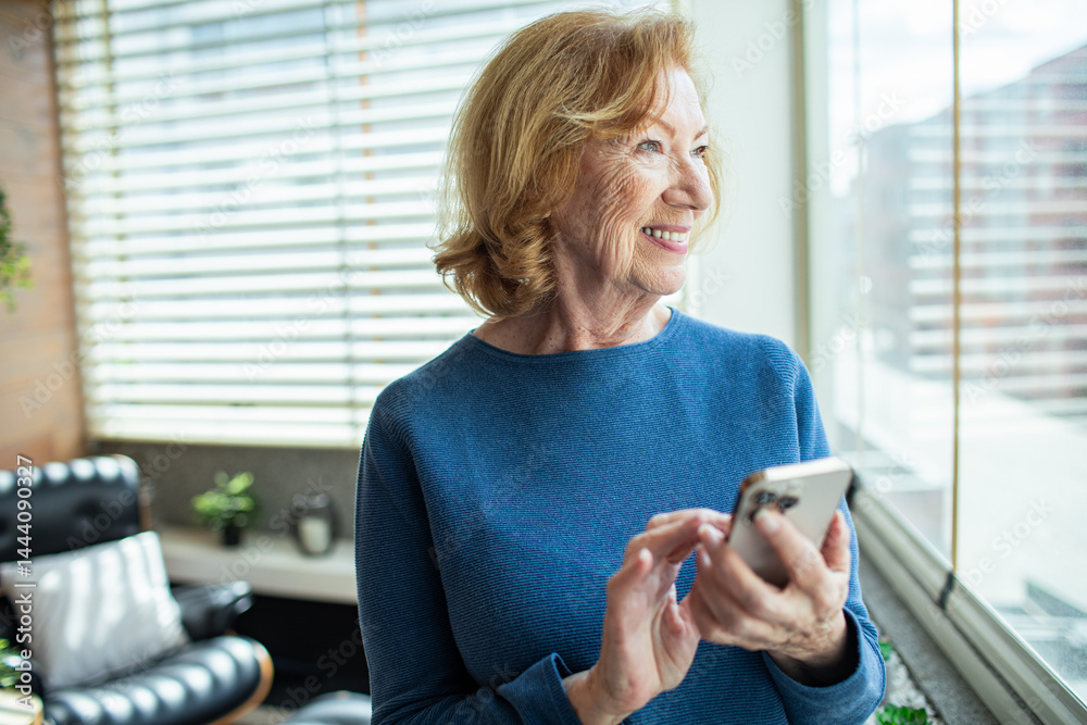 Senior woman smiling while using smartphone at home in bright living room