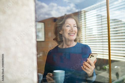 Obraz na płótnie Senior woman smiling while using smartphone at home in bright living room w salonie