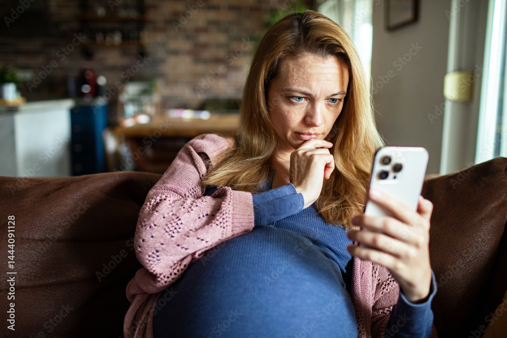 Pregnant woman using mobile banking app on smartphone while relaxing on couch