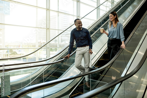 Escalator, talking and luggage with business people in airport together for travel or trip. Collaboration, smile and suitcase of man employee with woman colleague in lobby for international flight