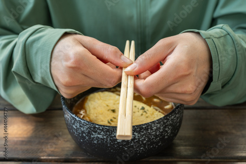Obraz na płótnie Cropped shot view of woman holding chopsticks before eating Udon. Udon is a thick, white, ribbon-like noodle popular in Japanese cuisine. w salonie