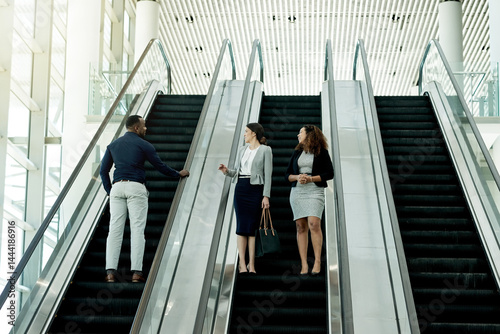 Office, walking and business people on escalator in lobby for meeting, discussion and networking. Professional, corporate and men and women at conference, convention and seminar in modern building