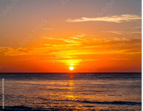 Fiery sunset over calm ocean. Golden hour colors paint the sky and sea.