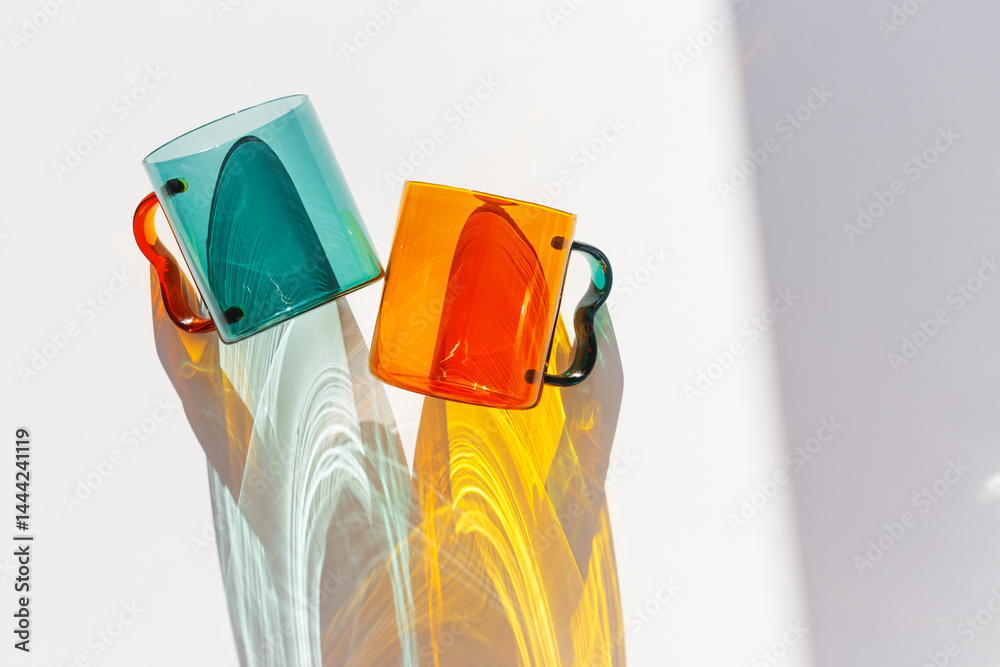 Orange and green Glass Mugs with bright sunlight Shadows, transparent cups casting dynamic, vibrant lights reflections and shadows on light white, creative aesthetic top view, minimal style, closeup