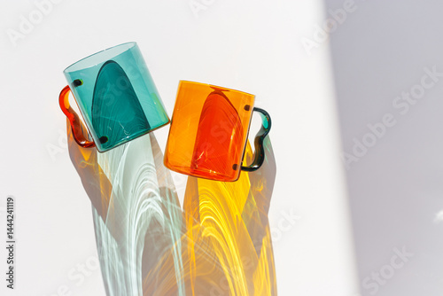 Obraz na płótnie Orange and green Glass Mugs with bright sunlight Shadows, transparent cups casting dynamic, vibrant lights reflections and shadows on light white, creative aesthetic top view, minimal style, closeup w salonie