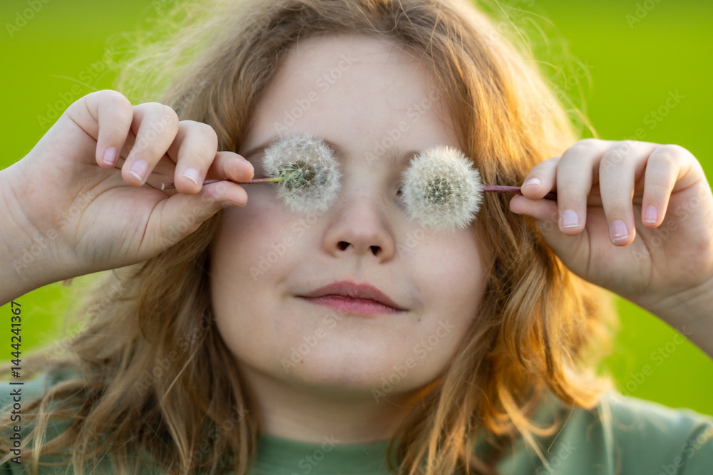 Kid face with dandelion cover eyes. Summer funny kids portrait close-up. Kid play with dandelions. Kid enjoys the carefree and hold dandelion near face. Kids freedom. Kids dreaming face.