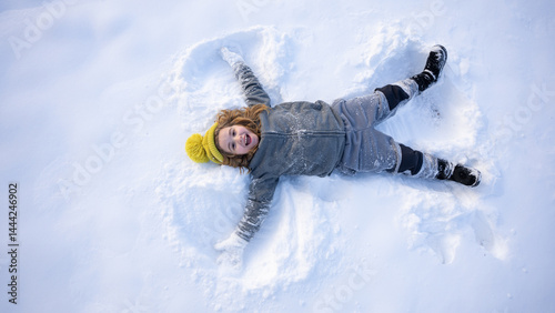 Child making a snow angel. Happy kid lying in the snow. Kid angel in snow. Winter kids with snowy angel wings. Smiling child on a snowy day. Carefree kid in the snow lake angel. Christmas joy.