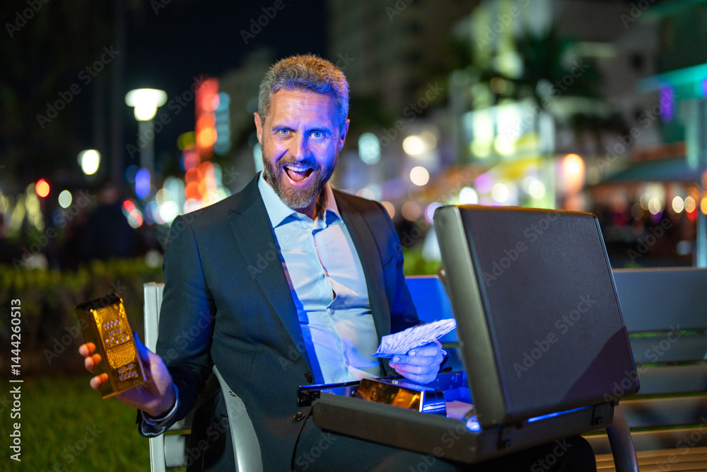Rich man holding a gold bar. Businessman with stacks of money and gold. Gold bars and dollar bills in hand. Wealthy man on bench with gold and money. Businessman counting cash. Banknotes and goldbar.