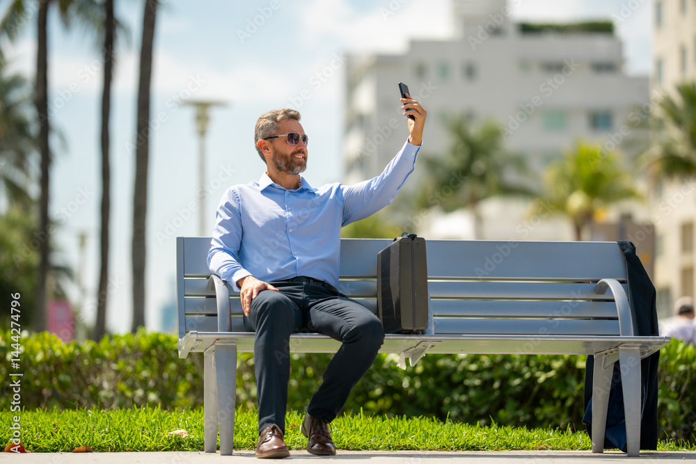 Successful business man working on a laptop outdoors. Confident business man sitting on a bench with a laptop. Hispanic business man working remotely. Rich business man working online in summer.