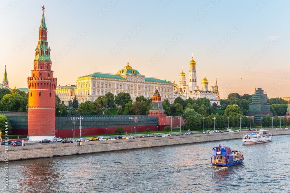 View of Kremlin with Vodovzvodnaya tower, Grand Kremlin Palace from repaired Bolshoy Kamenny Bridge in Moscow city on sunny summer day. Cruise ship sails on the Moscow river