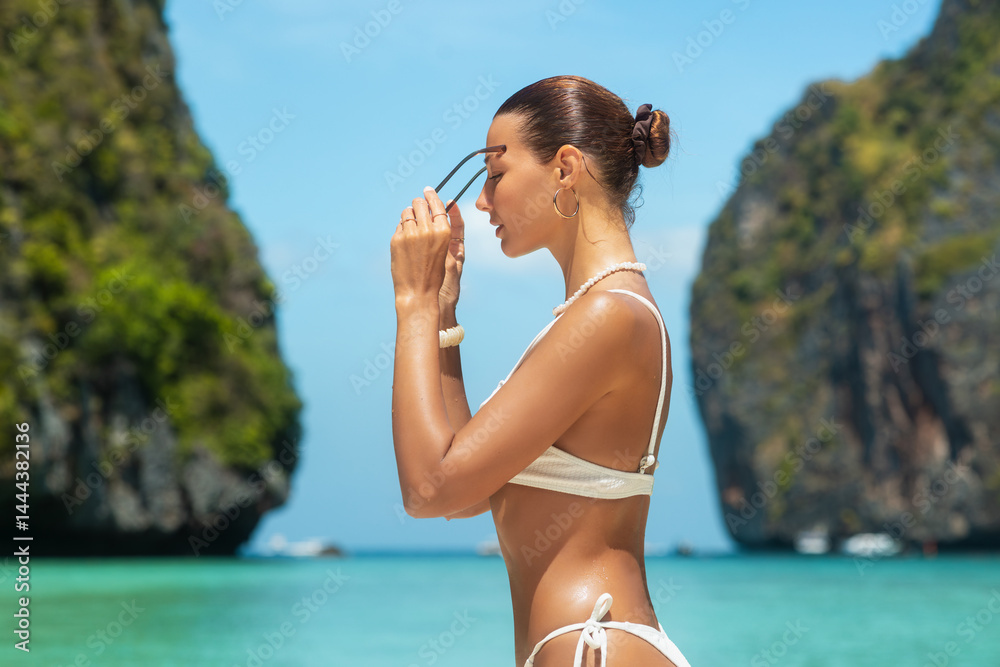 Elegant woman with glowing skin and slim figure adjusting sunglasses in profile view at tropical Maya Bay beach, Thailand, concept of luxury travel, fashion, summer promo, high quality lifestyle use.