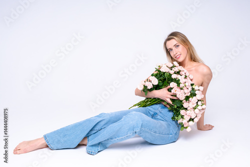 A young woman in jeans sits barefoot, hugging a lush bouquet of soft pink roses. Light atmosphere, a symbol of tenderness and freshness, a photo shoot in the studio