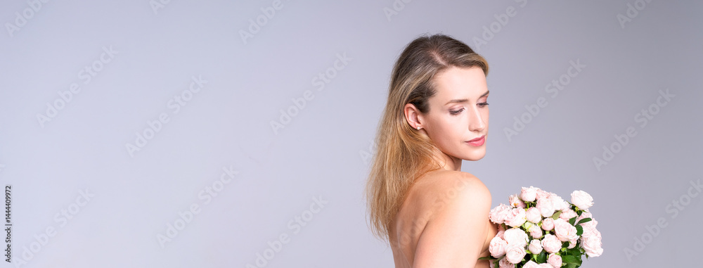 Delicate young woman with natural makeup holding flowers in bright studio, highlighting natural beauty and freshness of skin for self-care advertisement